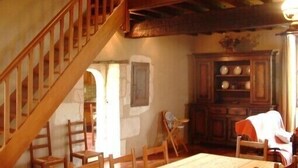 Una habitación rústica con una escalera de madera, una mesa de comedor y un aparador con vajilla.