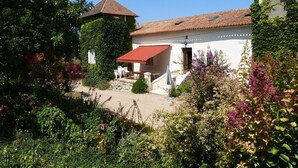 Una casa con toldo rojo, tejado de baldosas y jardín con diversas plantas y flores.