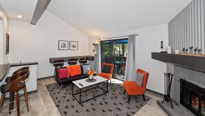 Un salon moderne avec une cheminée, un coin repas avec des chaises, un canapé avec des coussins et une vue sur une terrasse extérieure, accessible par une porte vitrée.