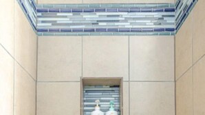 A tiled shower area with a shelf containing two bottles of Dove body wash.