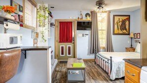 A compact room with a bed, a desk, a microwave, and a small table.