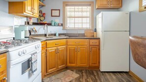 A kitchen with wooden cabinets, a white refrigerator, a stove, and a window with blinds.