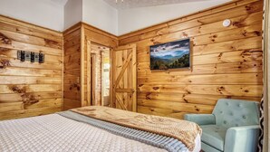 A wooden-paneled room with a bed, a light blue armchair, and a painting on the wall. - Smoky Mtn Cabin -Theater, Hot Tub, Games-9 min to Dollywood (Sevierville)