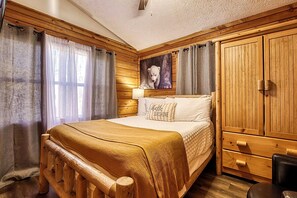 A wooden-paneled bedroom with a bed, curtains, a painting, and a wardrobe.