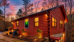 A log cabin with a porch, a painting, and a well-lit exterior at dusk. - Smoky Mtn Cabin -Theater, Hot Tub, Games-9 min to Dollywood (Sevierville)