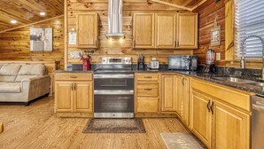 A wooden cabin interior with a kitchen featuring wooden cabinets, a stainless steel oven, and a granite countertop. - Smoky Mtn Cabin -Theater, Hot Tub, Games-9 min to Dollywood (Sevierville)