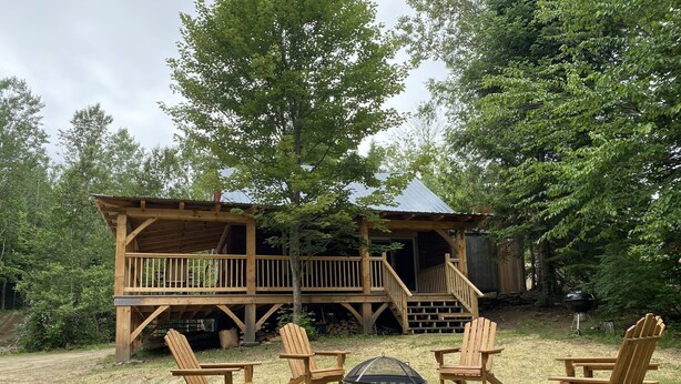 A wooden cabin with a deck, surrounded by trees. There are four Adirondack chairs and a black grill in the foreground. - Secluded trailside cabin for 8 people on Kingdom Trails  (Burke)