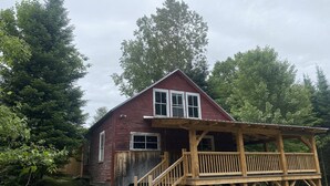 A rustic wooden cabin with a wooden deck and stairs leading to a covered porch. - Secluded trailside cabin for 8 people on Kingdom Trails  (Burke)