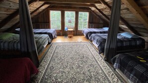 A cozy attic bedroom with two beds, a rug, and a window. - Secluded trailside cabin for 8 people on Kingdom Trails  (Burke)