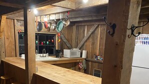 A rustic kitchen with wooden bar stools, a sink, and hanging pots. - Secluded trailside cabin for 8 people on Kingdom Trails  (Burke)