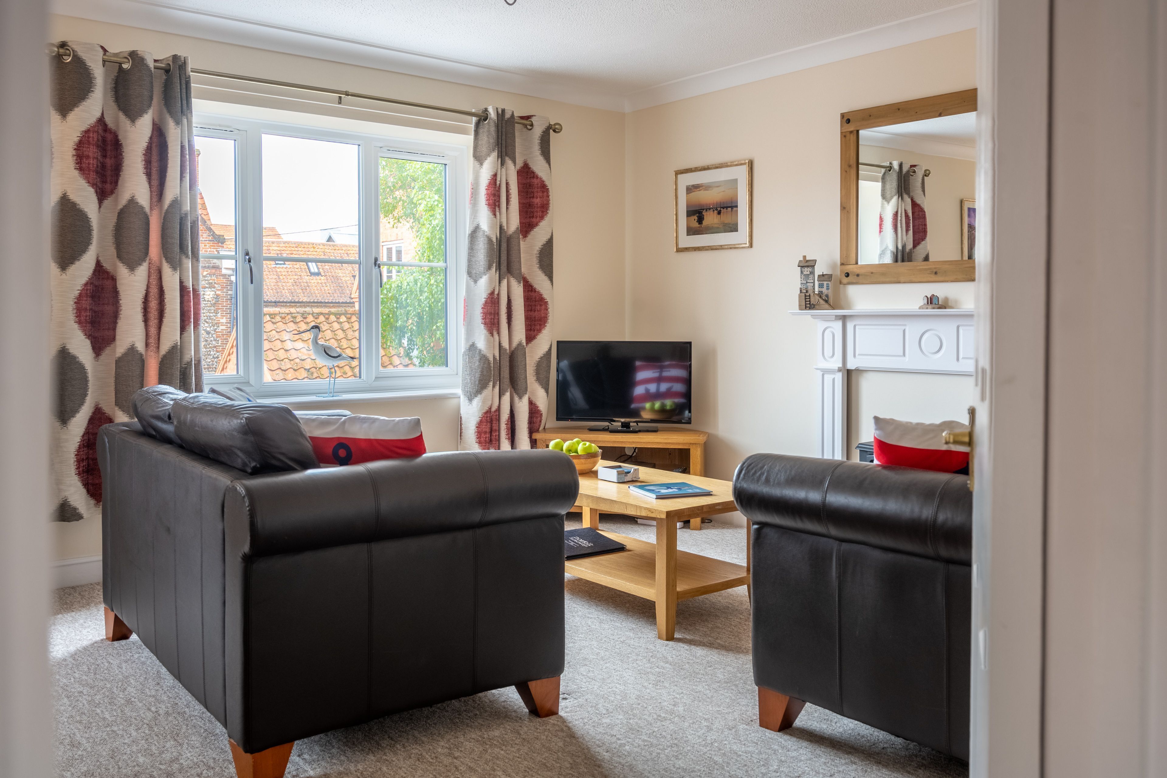 A living room with two black leather sofas, a wooden coffee table, a TV, and a window with patterned curtains.