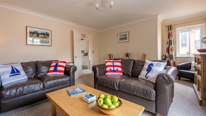 A living room with two leather sofas, a wooden coffee table with a bowl of apples, and a framed picture on the wall. - Avocet Apartment, Wells-next-the-Sea, Norfolk (Wells-Next-The-Sea)