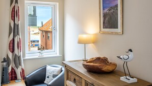 A room with a view of a building through a window, a lamp, a wooden bowl, and a bird sculpture. - Avocet Apartment, Wells-next-the-Sea, Norfolk (Wells-Next-The-Sea)