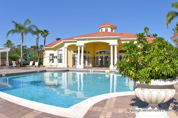 A pool area with a large pool, lounge chairs, and a building with a red roof.