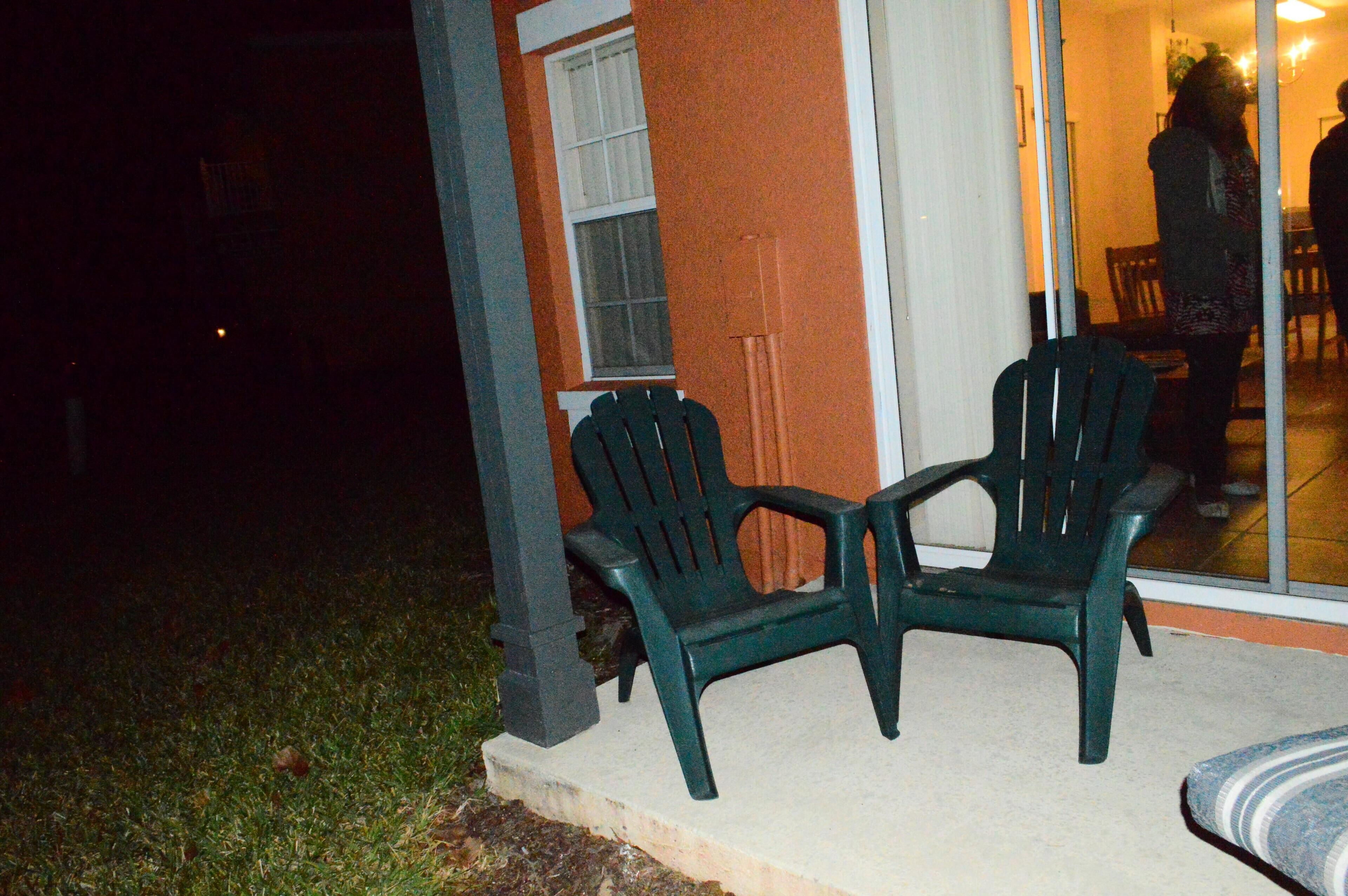 Two green plastic chairs outside a building with a glass door.