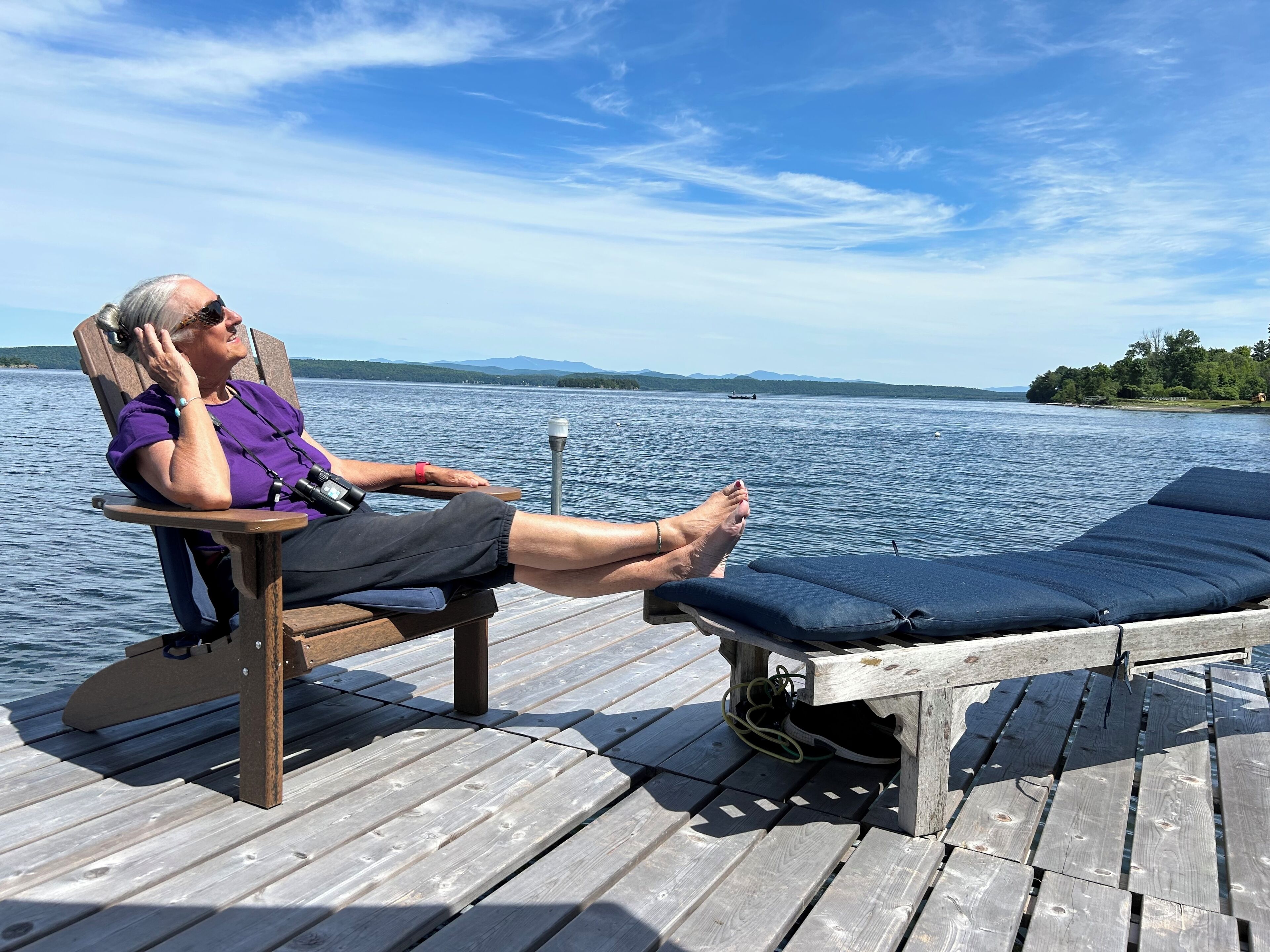 Une terrasse en bois avec un fauteuil et une chaise longue donnant sur un lac.