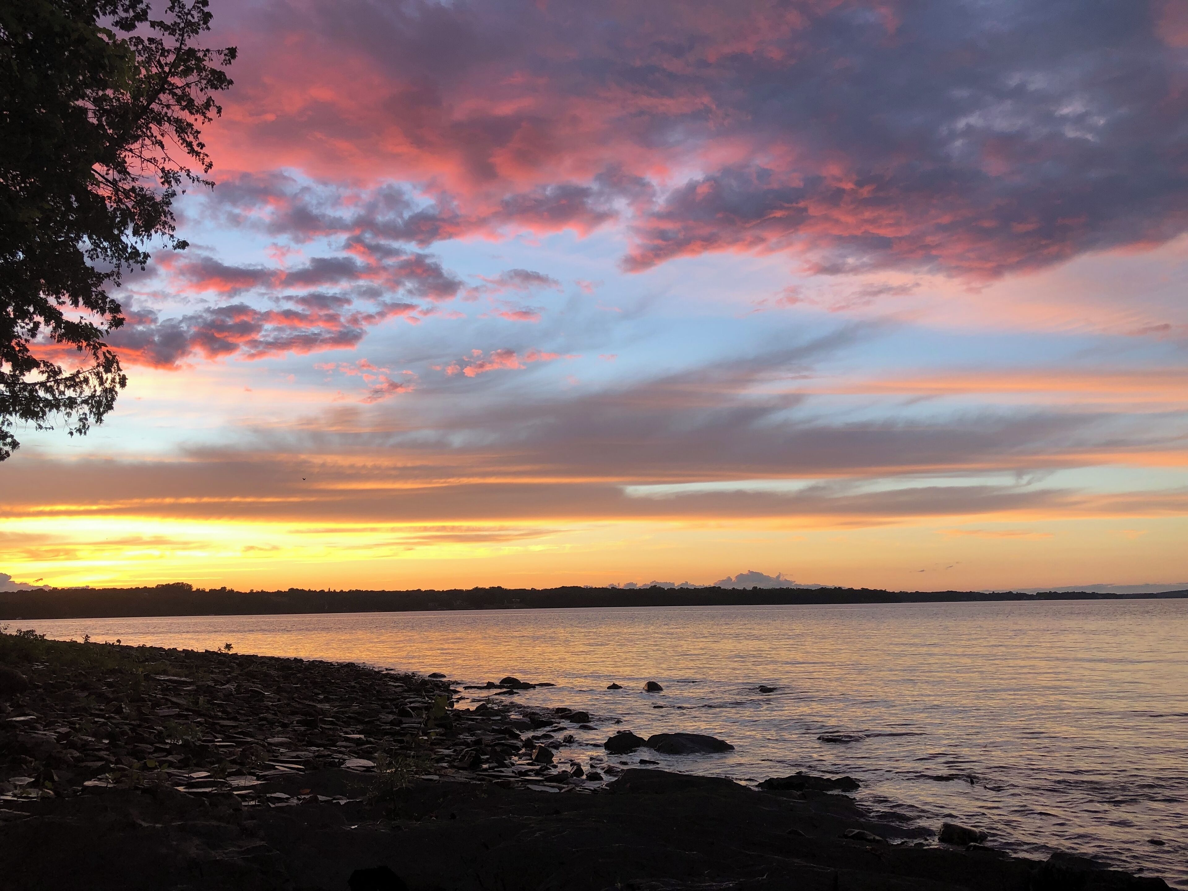 Solnedgang over en klippefyldt kystlinje med udsigt til fjerne bjerge.
