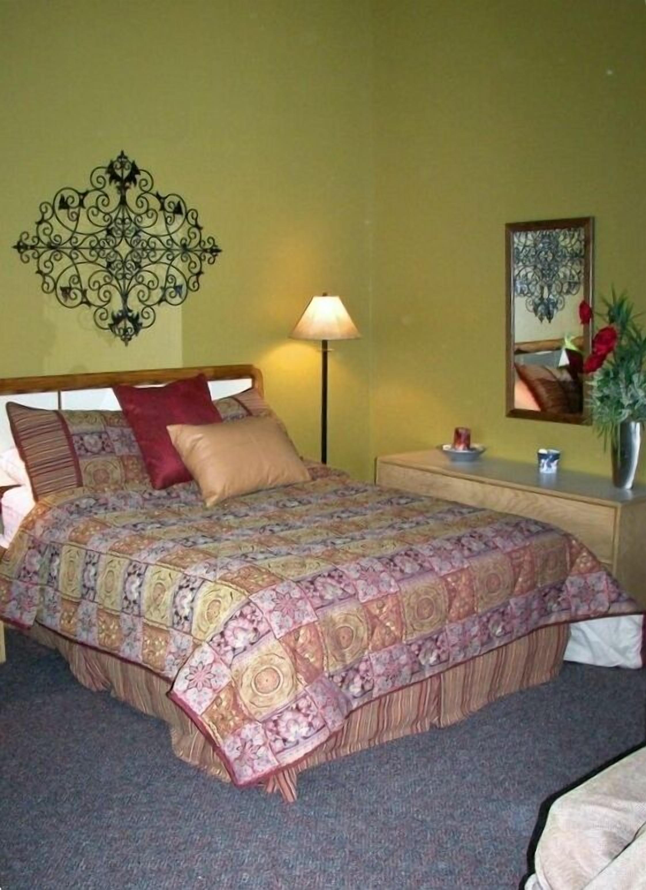 Une chambre à coucher comprenant un lit, une table de chevet, une lampe, un miroir et un élément décoratif mural.