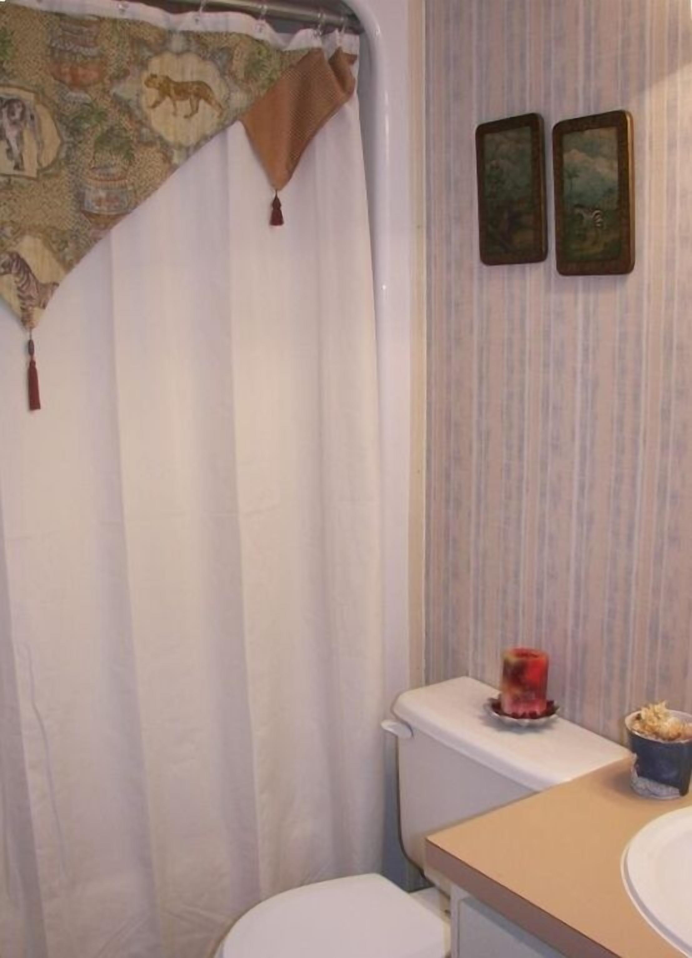 A bathroom with a shower curtain, toilet, and a sink with a candle.