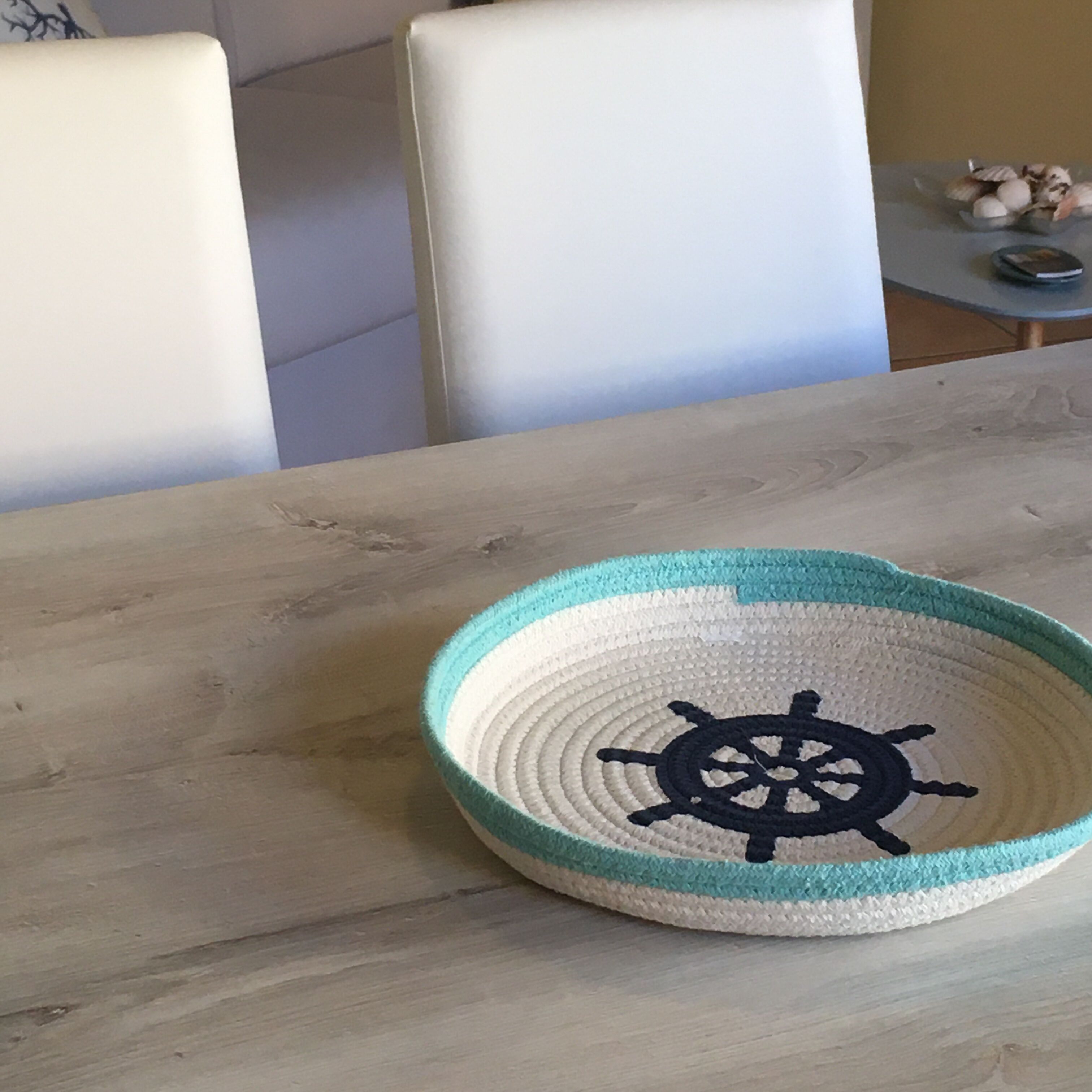 A woven tray with a ship's wheel design on a wooden table.
