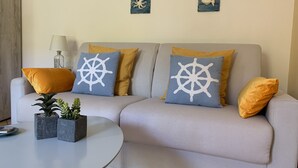 Una sala de estar con un sofá gris, dos cojines con motivos náuticos, una mesita con plantas y una lámpara.