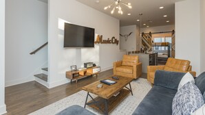 A modern living room with a staircase, a flat-screen TV, leather sofas, and a wooden coffee table. - Rooftop+Downtown close*  Nashville mural* (Nashville)