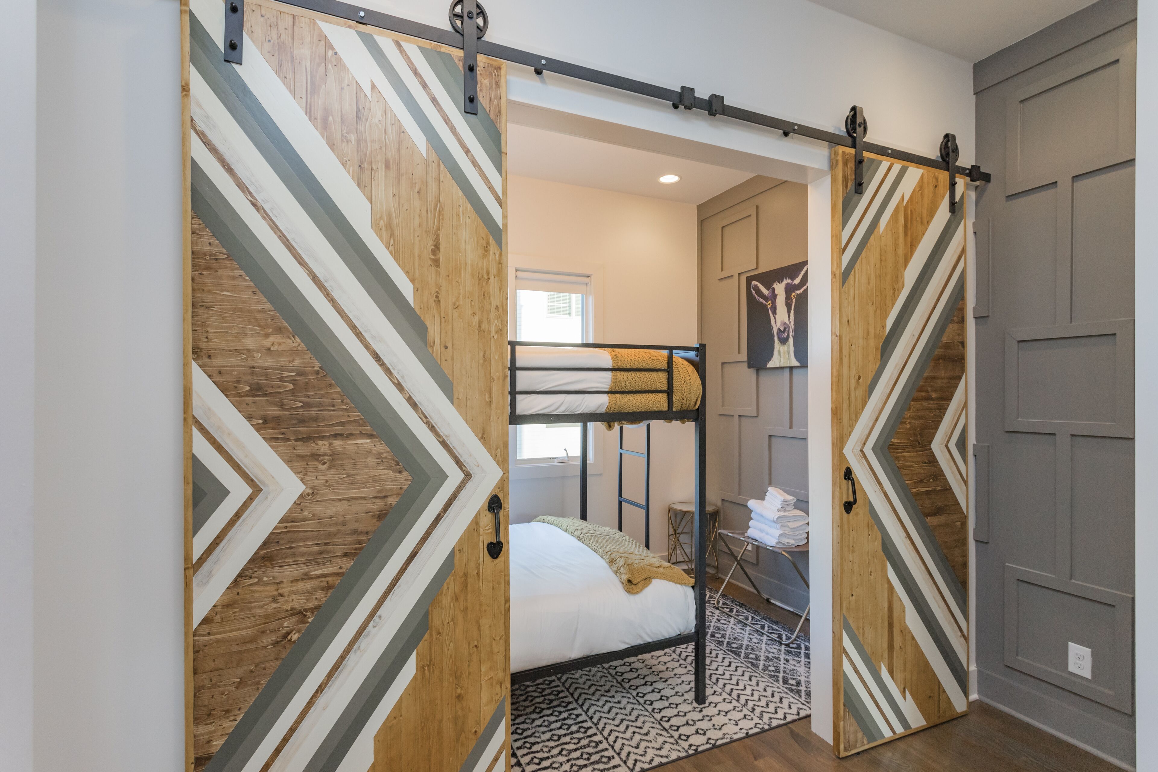 Ein Zimmer mit Etagenbett, einer Schiebetür mit geometrischen Mustern, einem gemusterten Teppich und einem kleinen Schreibtisch mit Stuhl.