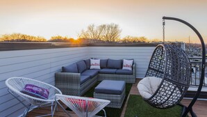 A rooftop patio with a sectional sofa, two chairs, a hanging chair, and a small table. - Rooftop+Downtown close*  Nashville mural* (Nashville)