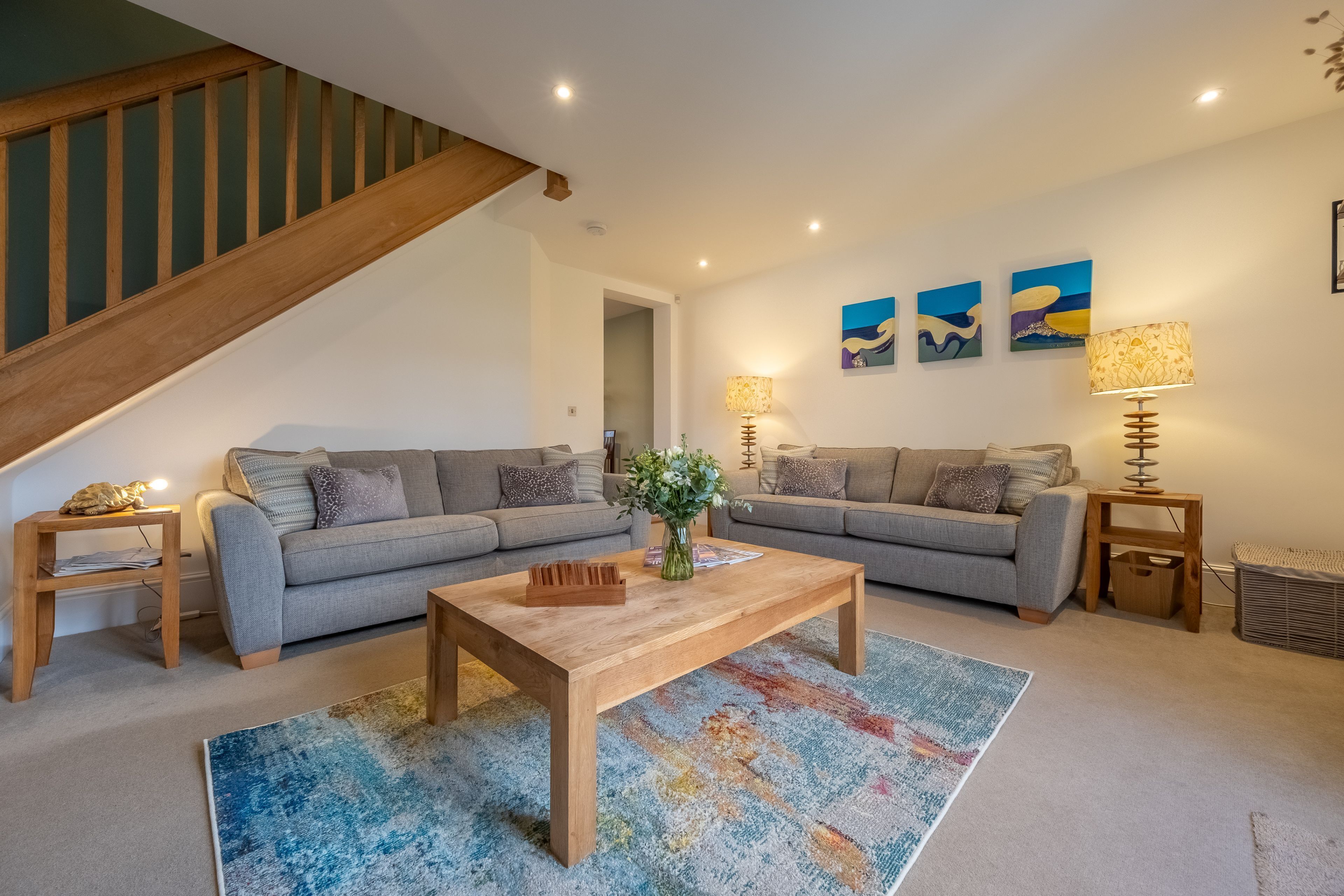 A living room with two grey sofas, a wooden coffee table, a colorful rug, and a staircase.