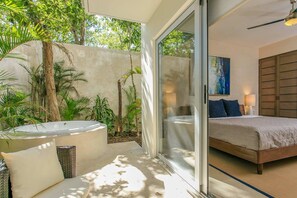 A bedroom with a large bed, a glass door leading to a patio with a hot tub and outdoor furniture.
