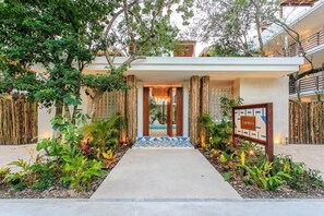 Welcome to a serene oasis surrounded by lush greenery, with a pathway leading to a covered entrance.