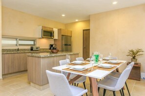 Une cuisine moderne avec un coin repas, comprenant un îlot central, des chaises blanches et une table dressée pour deux personnes.