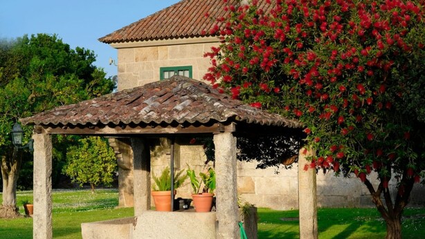 A stone building with a tiled roof, a pergola with potted plants, and a flowering bush. - Abadía Apartment, Rectoral of Areas (Tuy)