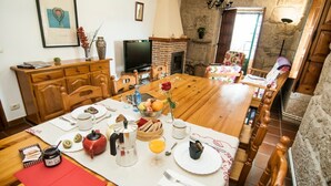 A dining area with a wooden table set for breakfast, a fireplace, and a stone wall. - Abadía Apartment, Rectoral of Areas (Tuy)