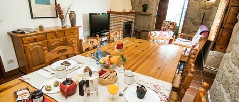 Un comedor con una mesa de madera dispuesta para el desayuno, una chimenea y una pared de piedra.