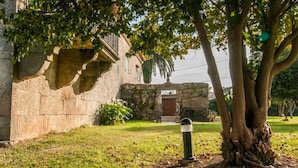 A stone building with a traditional design, a tree in the foreground, and a grassy area. - Abadía Apartment, Rectoral of Areas (Tuy)