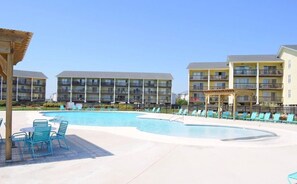 A hotel with a swimming pool, lounge chairs, and a covered seating area.