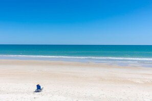 Ein Strand mit blauem Himmel, ruhiger See und einem einzelnen blauen Stuhl im Sand.