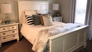 Une chambre à coucher avec un lit, deux tables de chevet, une commode et une fenêtre avec des rideaux.