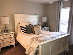 A bedroom with a bed, nightstands, lamps, and a window with curtains.
