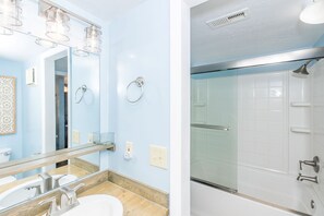 A bathroom with a mirror, sink, and shower.