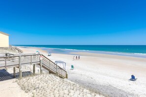 A beach with a wooden staircase leading down to the sand, a lifeguard tower, and beach chairs. - The Haven - Oceanfront Surf Condo! Community Pool, Sleeps 4 (Surf City)