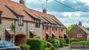 A row of terraced houses with pitched roofs, a car parked on the street, and a clear sky.
