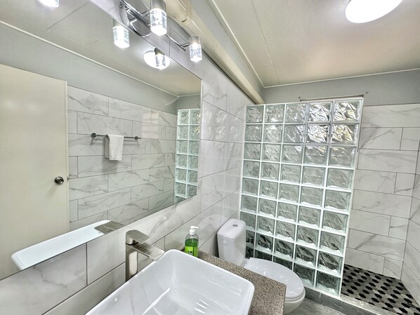 A modern bathroom with a large mirror, a white bathtub, a toilet, and a shower with frosted glass panels. - Updated/Beachfront/180 Sunset View/Dock/Dive Shop/Pool/Restaurants (Kralendijk)