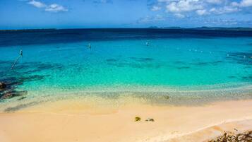 Une plage à l’eau turquoise et limpide, un rivage sablonneux et une terre lointaine à l’horizon.