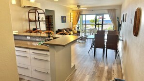A modern kitchen with a central island, a dining area with wicker chairs, and a view of the sea. - Updated/Beachfront/180 Sunset View/Dock/Dive Shop/Pool/Restaurants (Kralendijk)