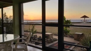 A room with a view of the beach at sunset, a dining table with chairs, and a small garden area with plants. - Updated/Beachfront/180 Sunset View/Dock/Dive Shop/Pool/Restaurants (Kralendijk)