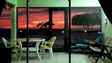 Une pièce avec une cloison en verre, des chaises blanches, une table et une vue sur un coucher de soleil, avec la silhouette d’une vache en arrière-plan.