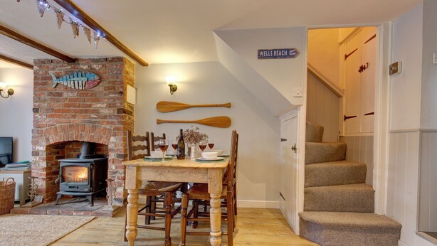Un salon chaleureux avec une cheminée en briques, une table à manger en bois et un escalier menant à l’étage supérieur.