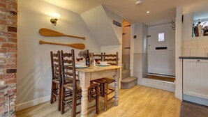 Un espace repas comprenant une table et des chaises en bois, un mur en briques et un plafond avec des poutres apparentes.